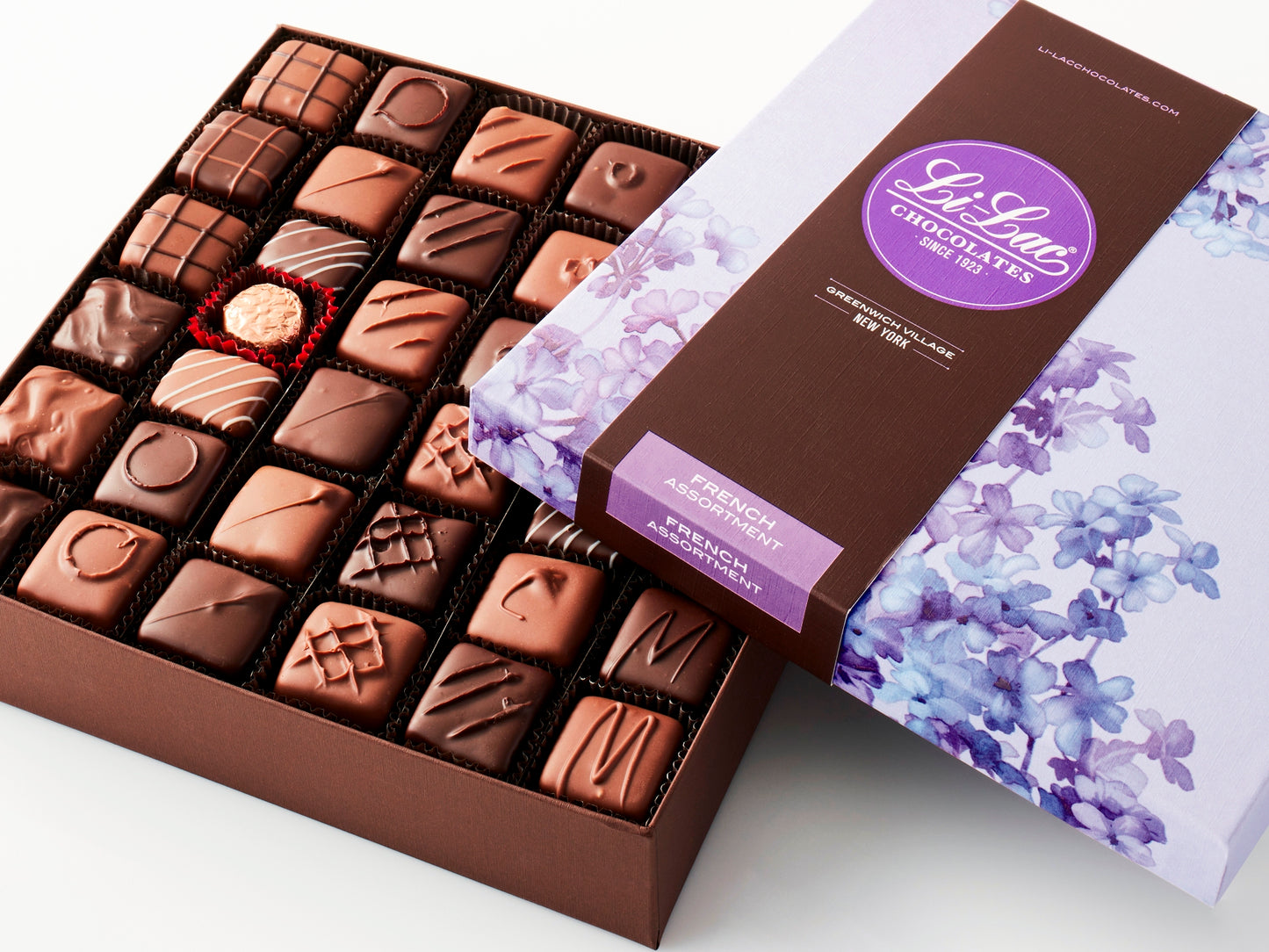 An open box displaying the chocolates inside with the cover partially covering the top showing a floral lilac pattern on the box top