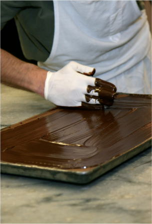 A gloved hand spreads chocolate on a rectangular surface