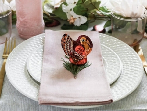 Chocolate Turkey sits on a sprig of evergreen decorating a place setting on a holiday table.