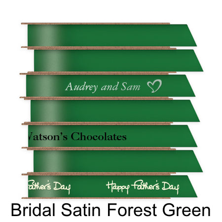 A stack of seven spools of shiny forest green satin ribbon with custom messages printed on them in different colors.