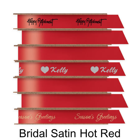 A stack of seven spools of shiny red satin ribbon with custom messages printed on them in different colors.