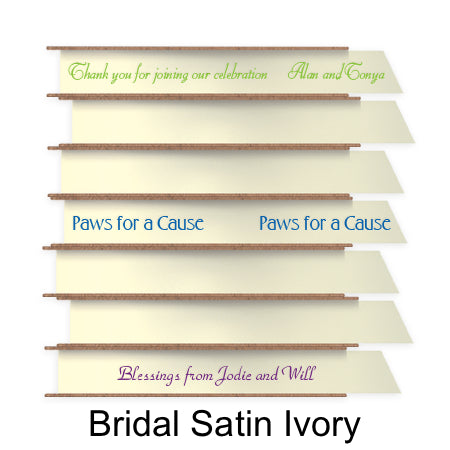 A stack of seven spools of shiny ivory satin ribbon with custom messages printed on them in different colors.