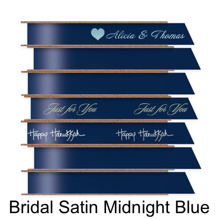 A stack of seven spools of shiny midnight blue satin ribbon with custom messages printed on them in different colors.