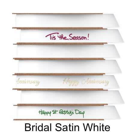 A stack of seven spools of shiny white satin ribbon with custom messages printed on them in different colors.