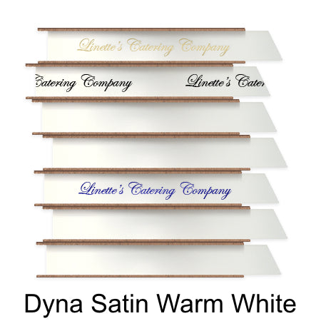 A stack of seven spools of shiny warm creamy white satin ribbon with custom messages printed on them in different colors.