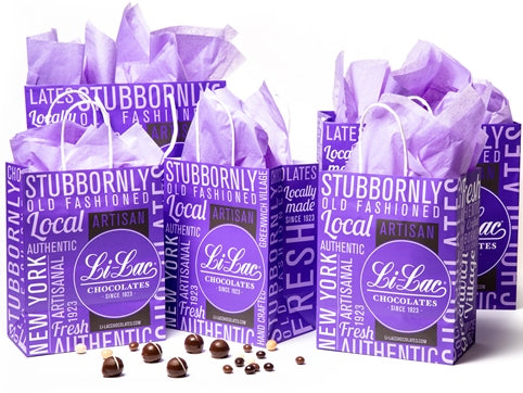 Handled gift bags in two sizes are assembled together. The bags feature the purple Li-Lac Chocolate logo and text branding all over, and have lilac purple tissue paper inside.