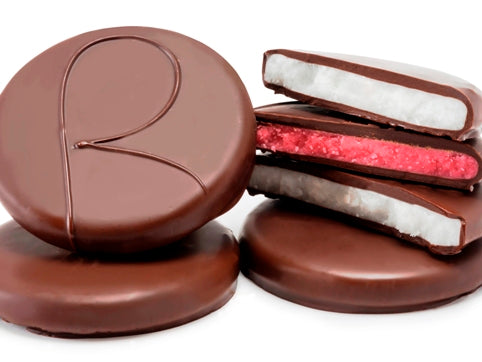 Flat, round disks of mint and raspberry soft cream are enrobed in dark chocolate. Several of the patties have been broken in half, reveling white mint cream centers and pink raspberry cream centers.