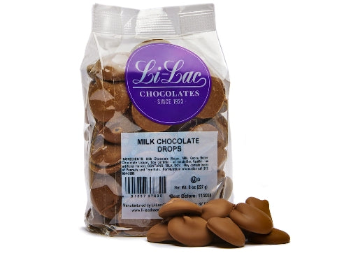 A clear cellophane bag of milk chocolate drops sits with a few chocolate drops scattered on the table next to it.