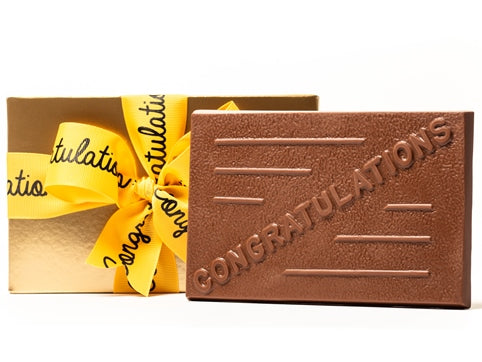 A large rectangular chocolate bar as the word 'Congratulations' written on it. It comes in a gold gift box with a yellow ribbon with Congratulations written on the ribbon in black script.