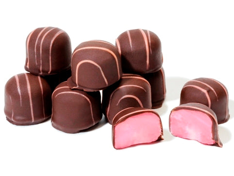 Mounds of raspberry soft cream are enrobed in dark chocolate with pink drizzle on top. One of the raspberry creams is cut in half reveling a soft pink raspberry cream center.