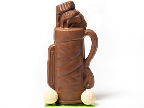 A molded chocolate Golf Bag has clubs coming out of the top and two white chocolate golf balls sitting next to the bag.