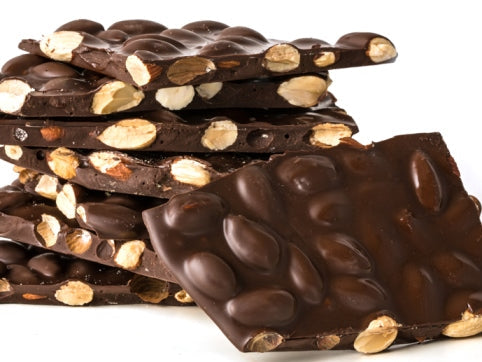Thin sheets of almond bark are shown in dairy free dark chocolate. The sheets are broken into pieces, exposing the toasted almonds inside. 