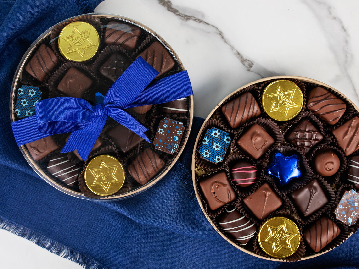 A round box filled with Chanukah chocolates next to the same box with a clear lid and blue ribbon.