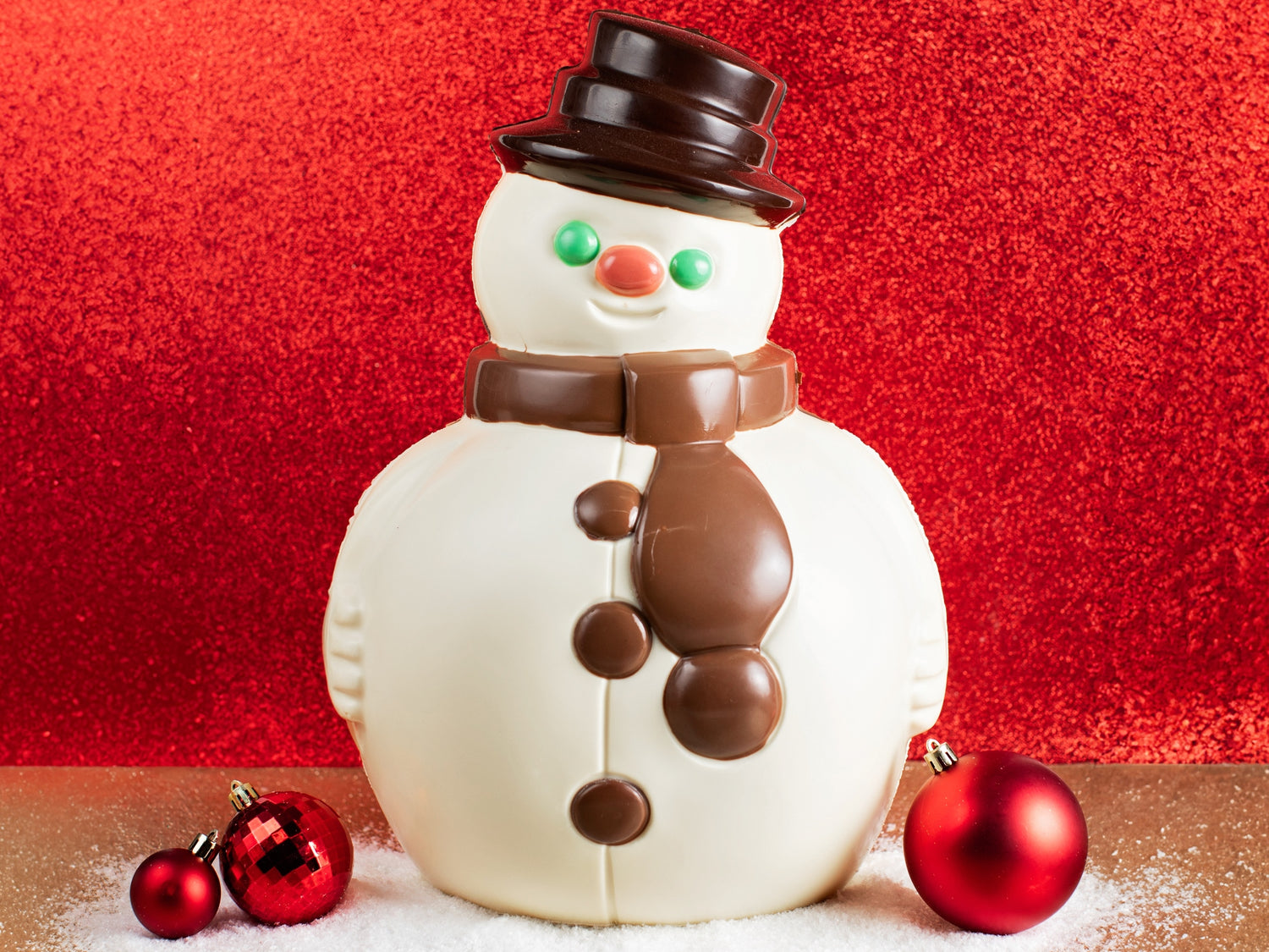 A large round white chocolate snowman has a milk chocolate scarf and a dark chocolate hat