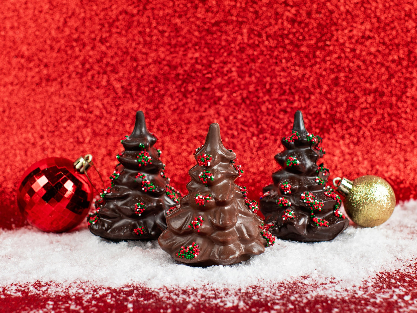 Three small chocolate molded evergreen trees with nonpareil seeds on the tree boughs in red and green.