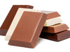 Small rectangular bars of milk, white and dark chocolate are stacked up together.